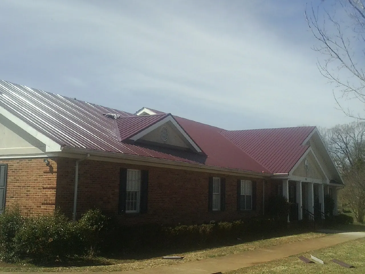 Red metal roof with gabled entries on a long brick building, from a Hail Damage Roof Repair job in Lyndonville
