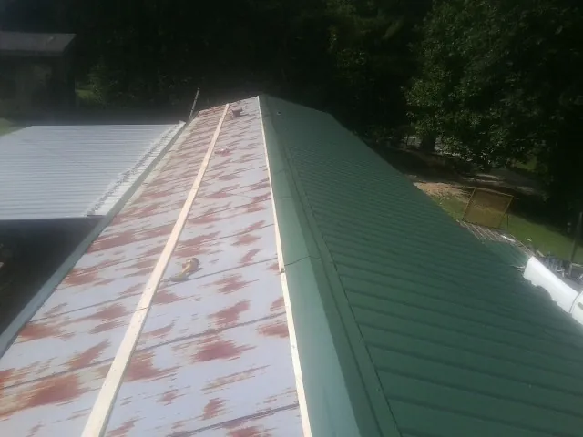Old rusted panels beside newly installed green metal roofing — Wind Damage Roof Repair by Roofing Brothers in Lyndonville