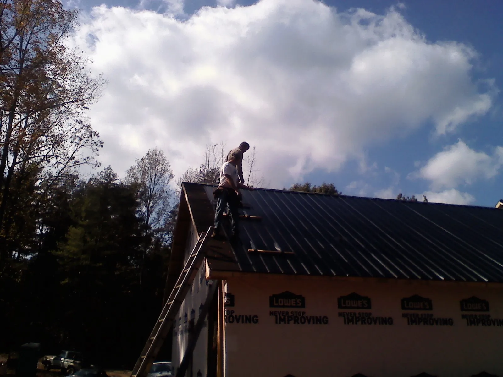 Roofer fastening dark metal panels high against a cloudy sky, from a Roof Inspection job in Lyndonville