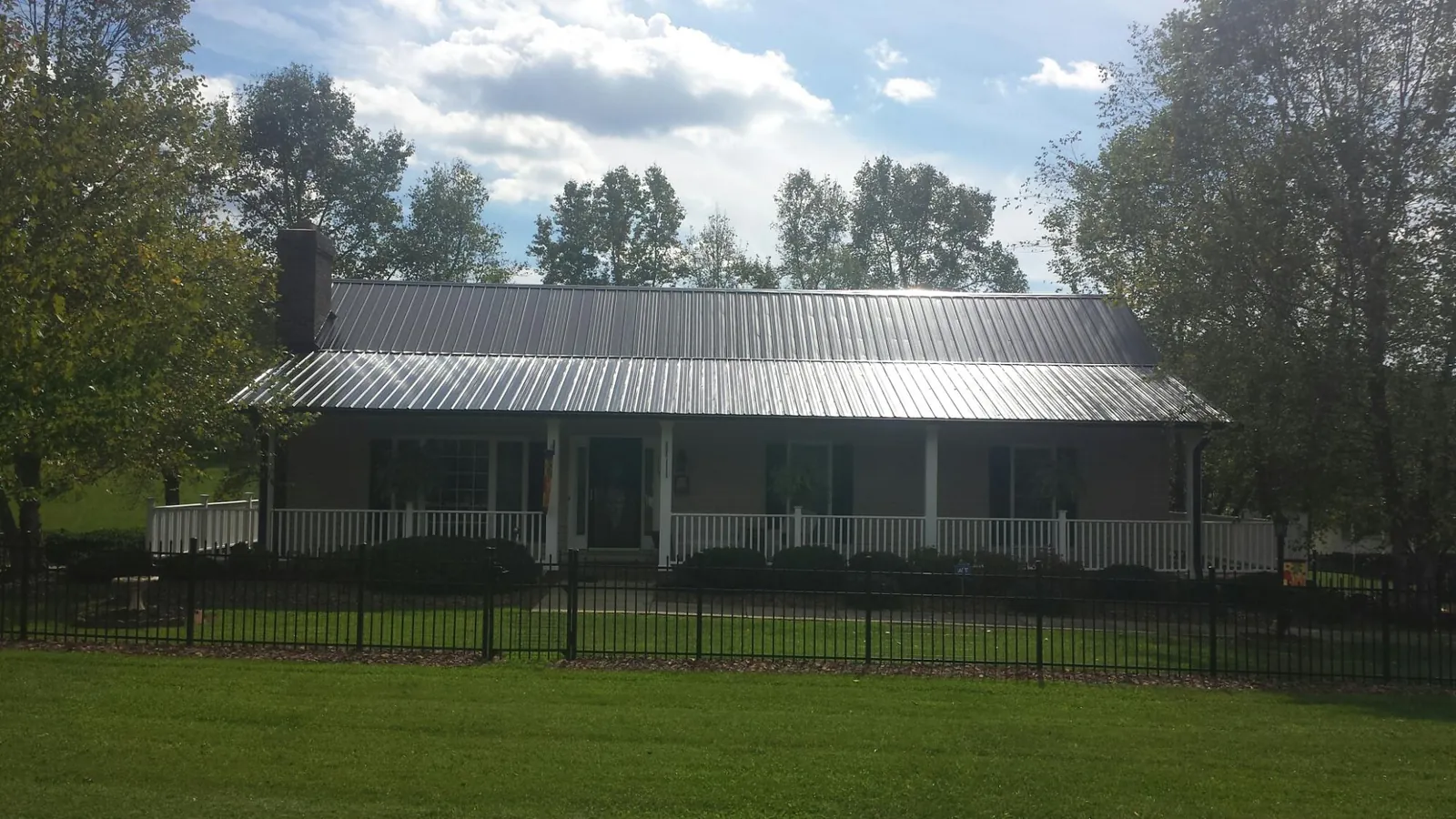 Gray metal roof on a brick ranch with a full width front porch — Gutter Guard Installation work by our crew in Lyndonville