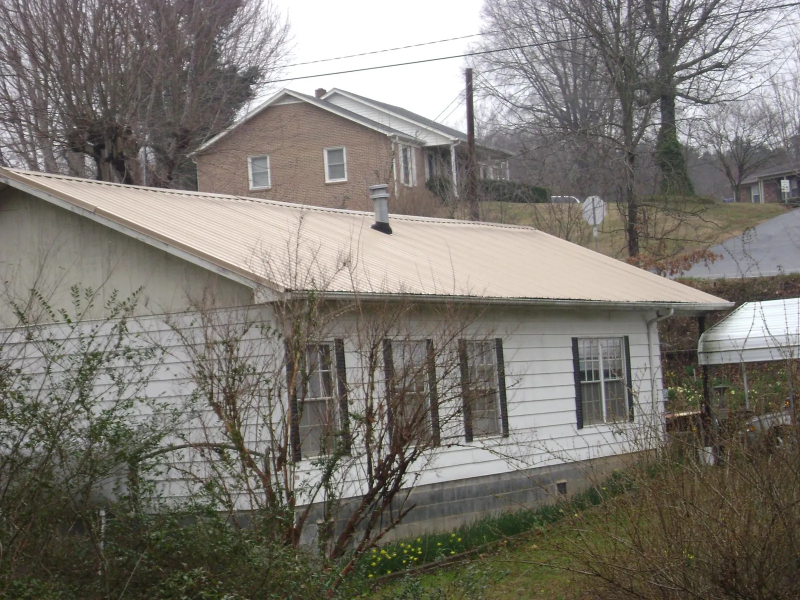 Tan metal roof on a white sided house set into a hillside — Commercial Roofing by Roofing Brothers in Lyndonville