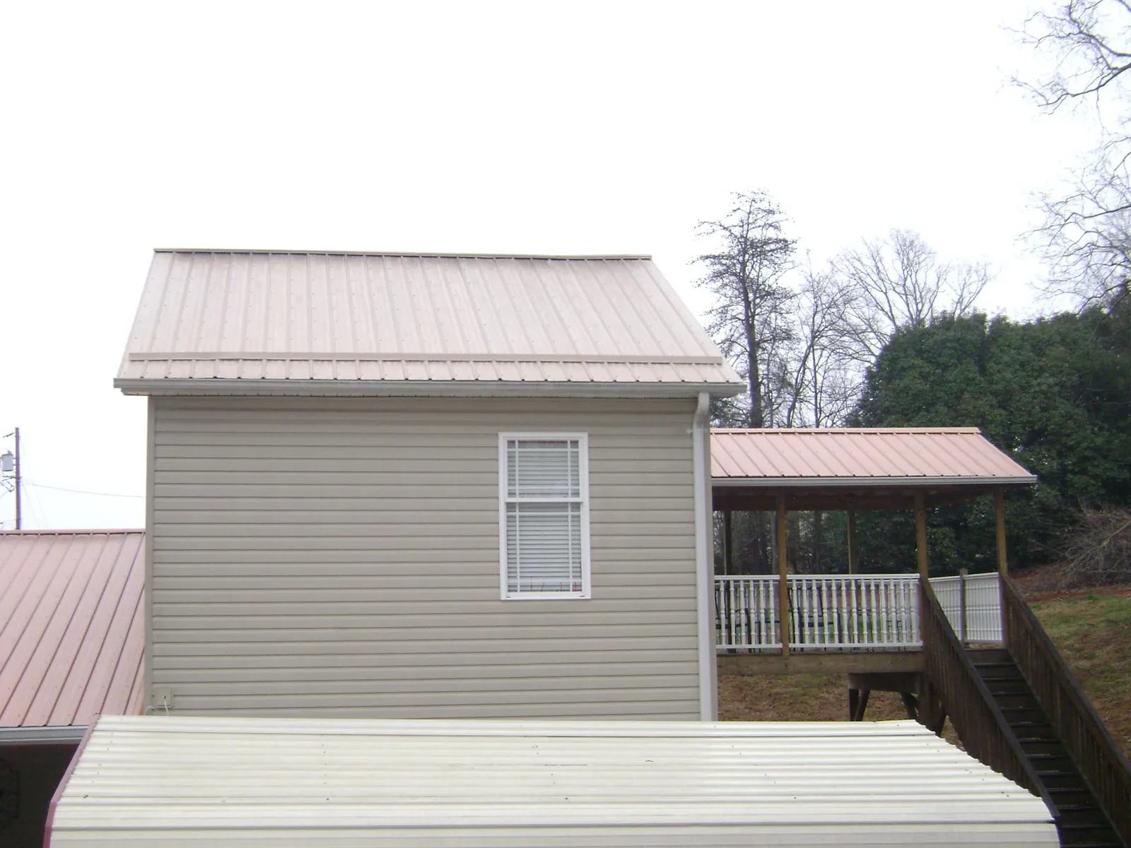 Tan metal roofs on a two story addition and attached porch, from a Roof Replacement job in Lyndonville